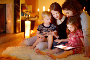 Happy young family using a tablet pc at home by a fireplace in warm and cozy living room on winter day