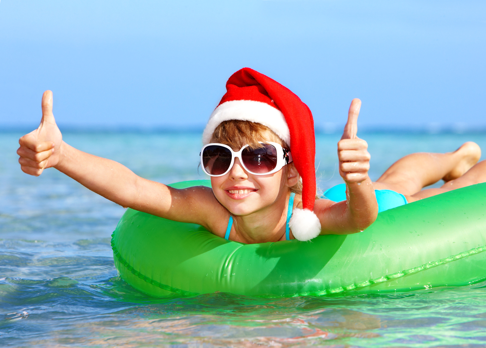 Child in santa hat  floating on inflatable ring in sea. Thumb up.